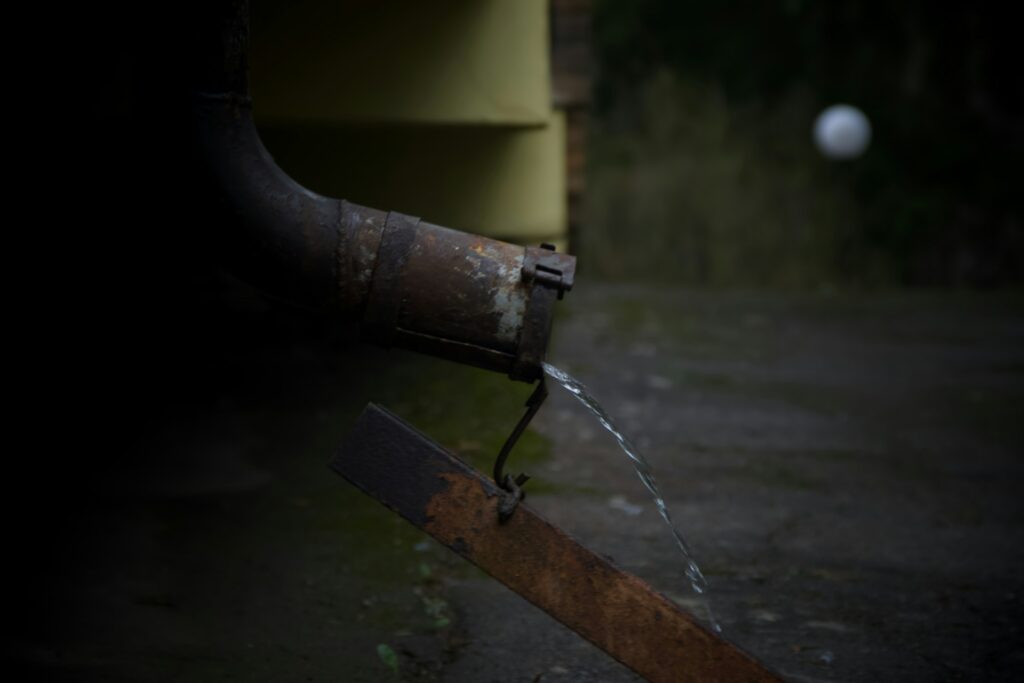 Rainwater dripping from a weathered metal downspout during the first steady fall rain in western Washington